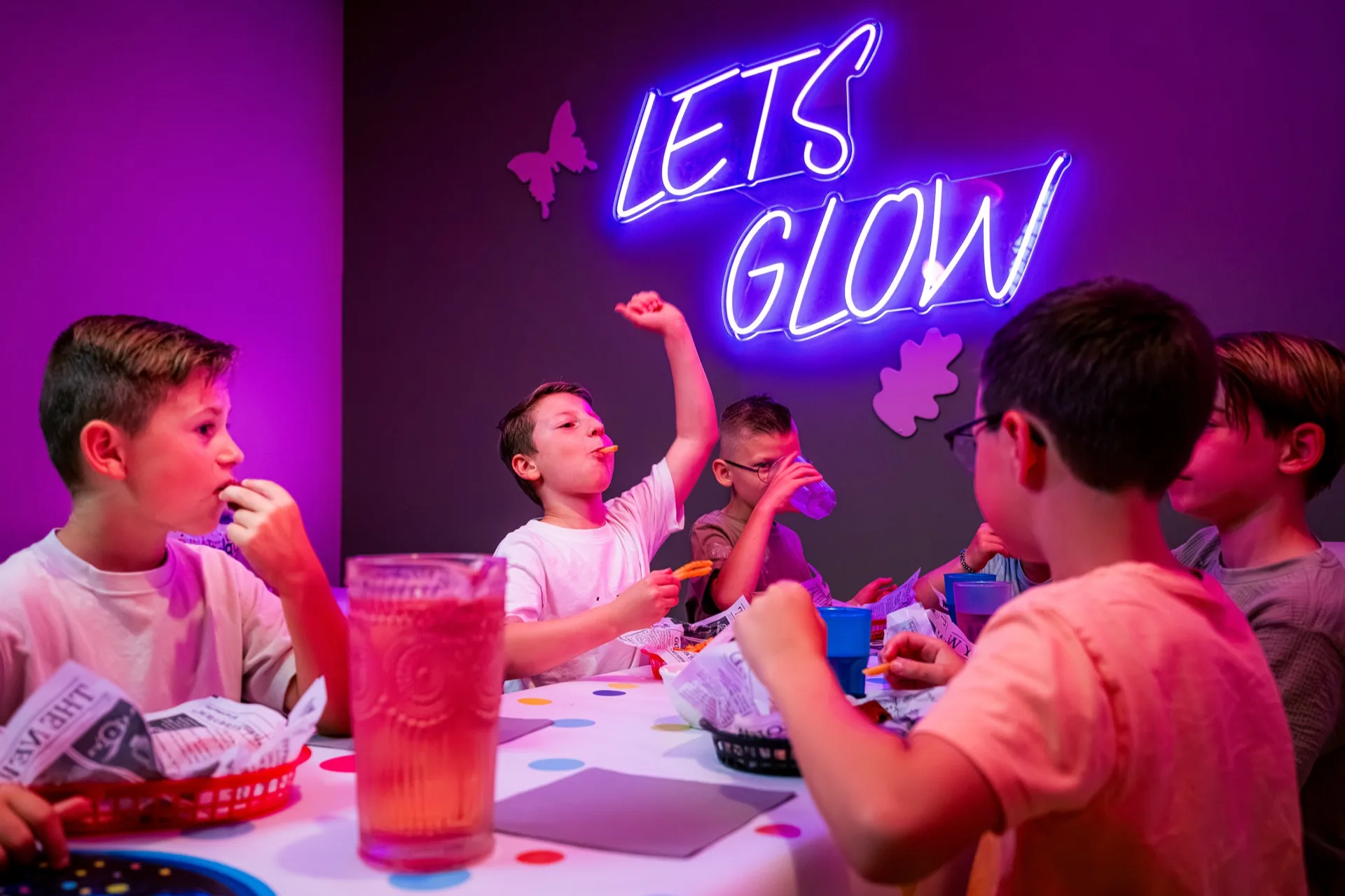 Kinderen eten friet en drinken ranja aan tafel onder de Lets Glow-neon bij een kinderfeestje in Kerkrade